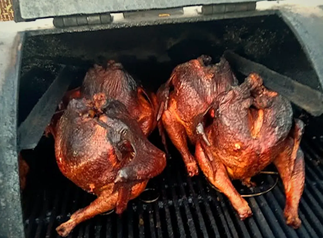 Two whole turkeys, deep mahogany from the smoke, inside the pit