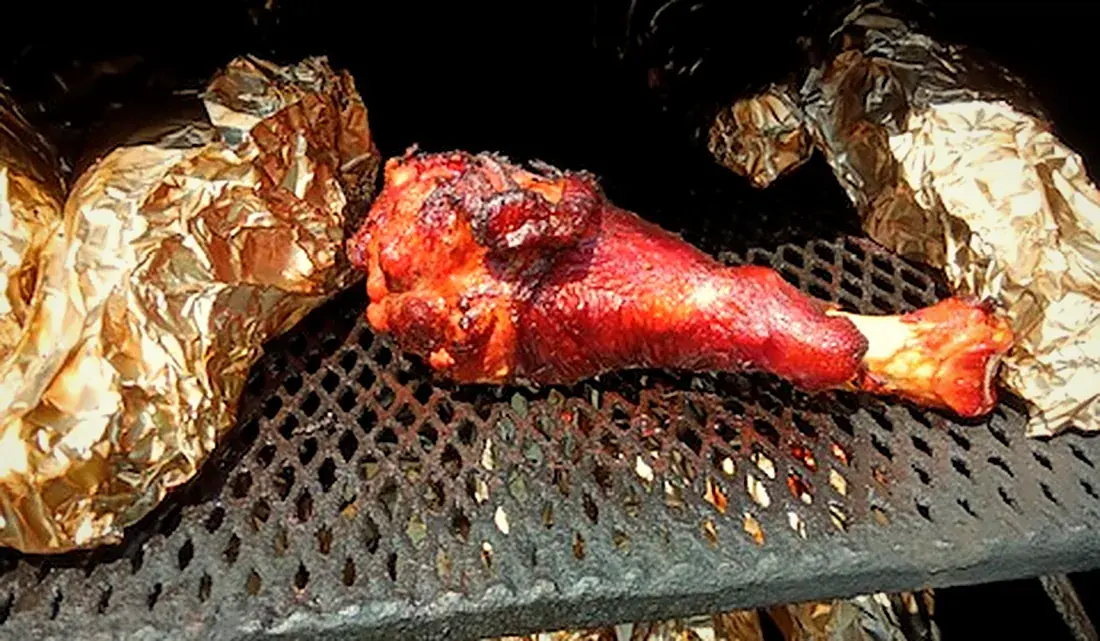 A glazed smoked turkey leg on the grate beside foil-wrapped sides
